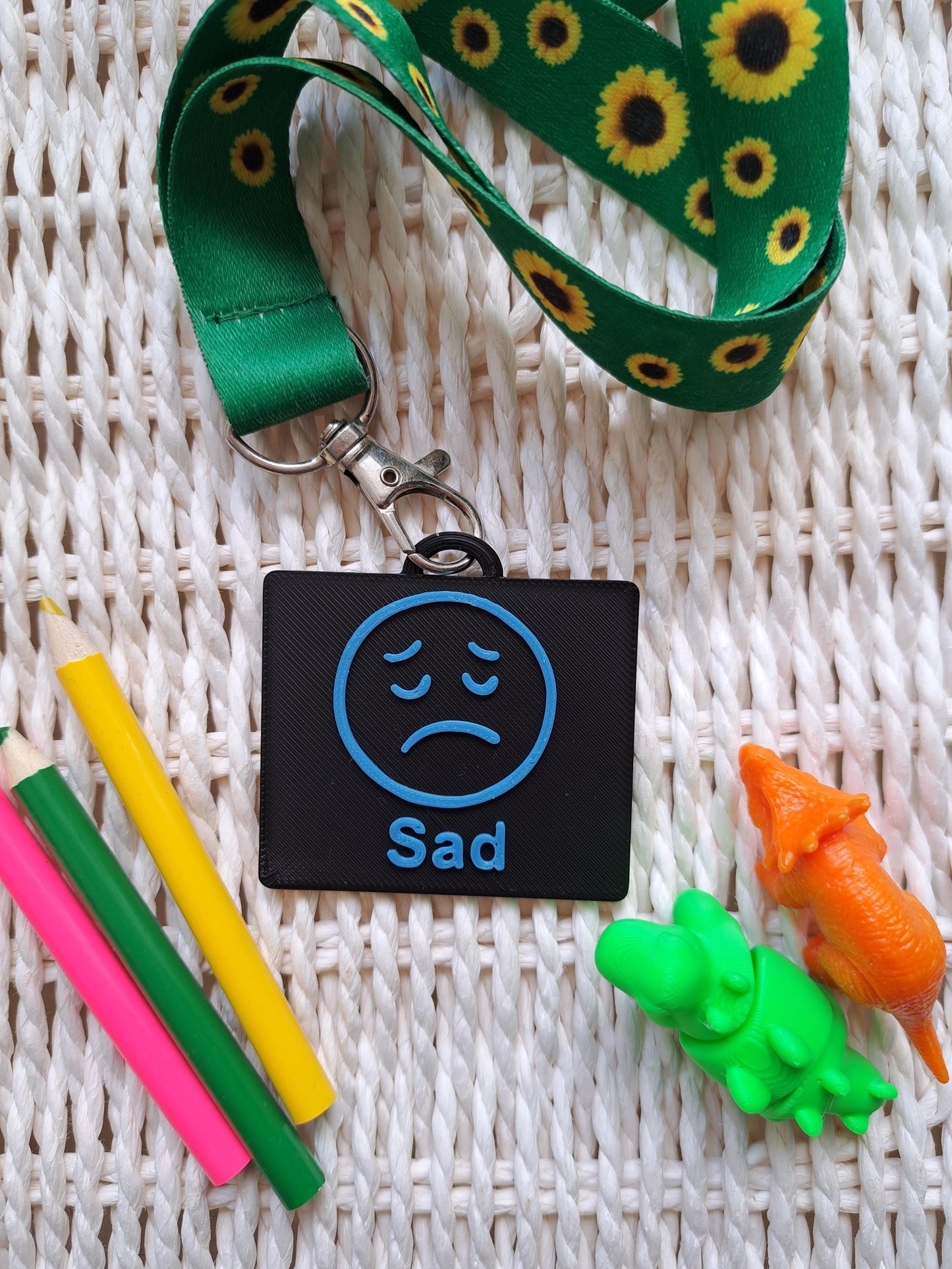 A black-colored 3D-printed communication tag with a raised blue "sad" face and the word "sad" below it. This visual aid tag is designed to support nonverbal communication, autism-friendly tools, and AAC needs.