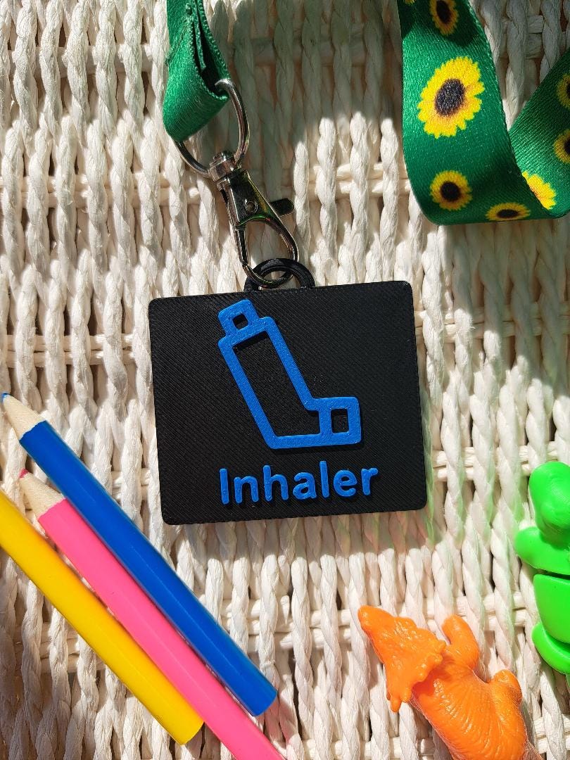 A black-colored 3D-printed communication tag with a raised blue inhaler with the words "Inhaler" below it. This visual aid tag is designed to support nonverbal communication, autism-friendly tools, and AAC needs.