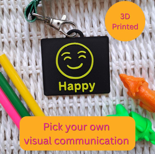 A black-colored 3D-printed communication tag with a raised yellow "happy" face and the word "happy" below it. This visual aid tag is designed to support nonverbal communication, autism-friendly tools, and AAC needs.