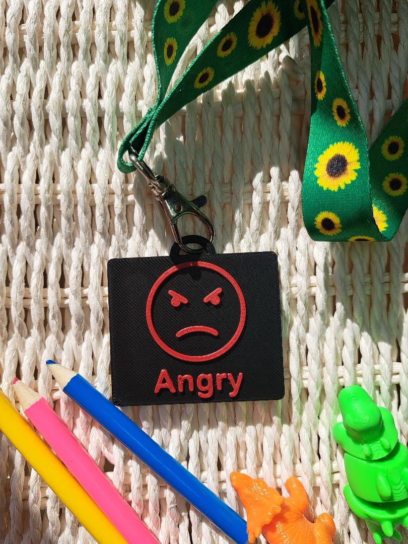 A black-colored 3D-printed communication tag with a raised res "angry" face and the word "angry" below it. This visual aid tag is designed to support nonverbal communication, autism-friendly tools, and AAC needs.