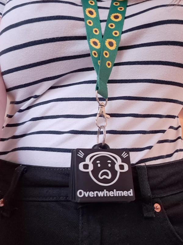 Person wearing a sunflower lanyard holding a set of 3D-printed autism communication tags clipped to their belt. The tags display emotions like "Overwhelmed" and "Happy," supporting non-verbal communication for autistic individuals, ADHD, and SEN users. Ideal for PECS, AAC, and sensory-friendly communication.