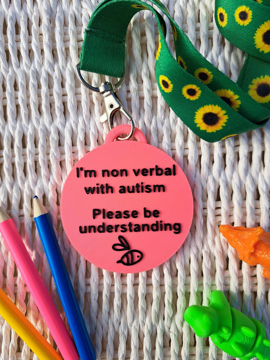 Autism ID Tag with 'I'm Non Verbal with Autism, Please Be Kind and Understanding' text, attached to a sunflower lanyard. Includes a black bee icon, surrounded by colorful pencils and sensory fidget toys. Ideal for autism awareness, backpacks, and lanyards.