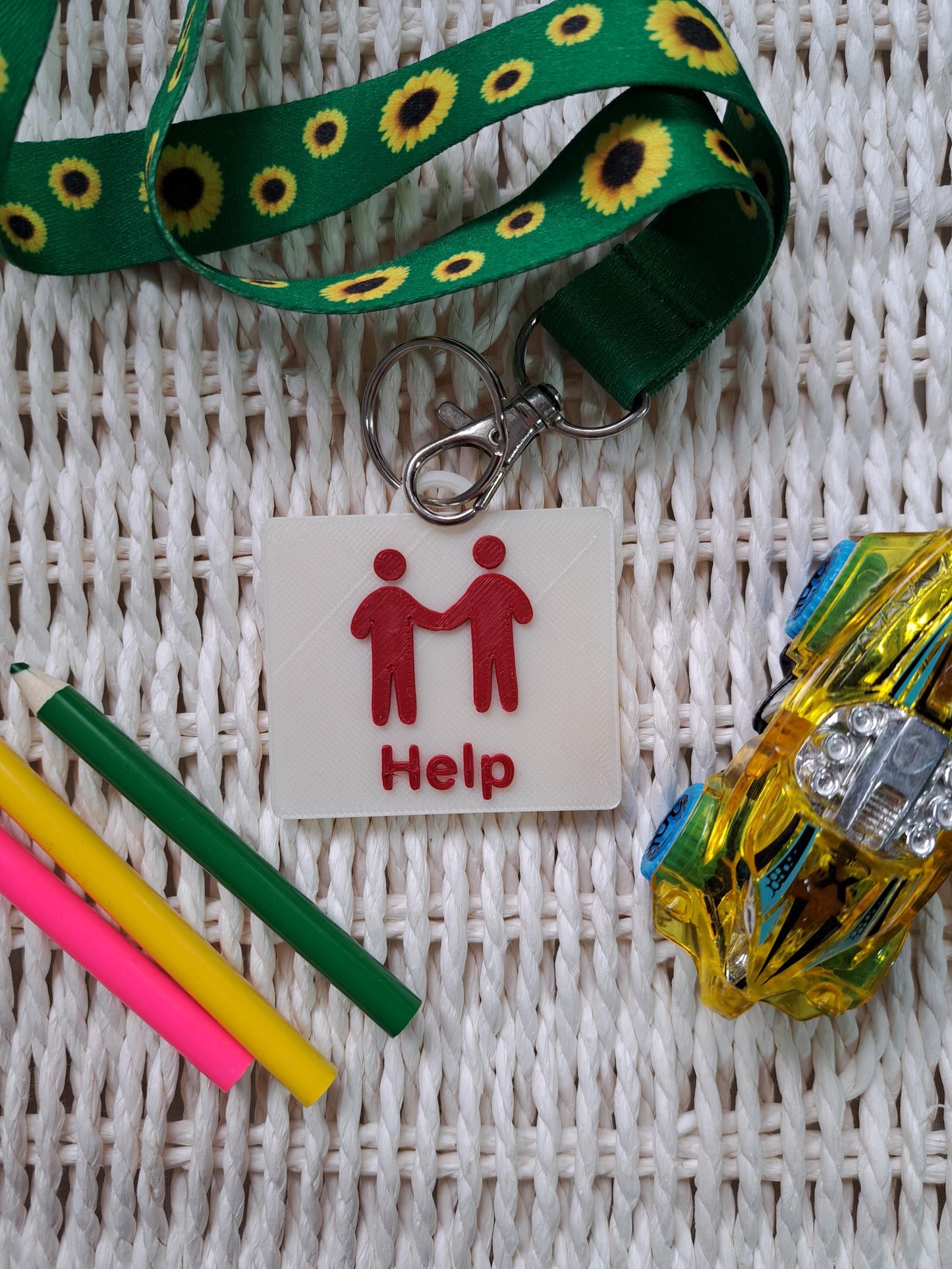A cream-colored 3D-printed communication tag with a raised red "help" symbol featuring two people holding hands and the word "Help" below it. This visual aid tag is designed to support nonverbal communication, autism-friendly tools, and AAC needs.