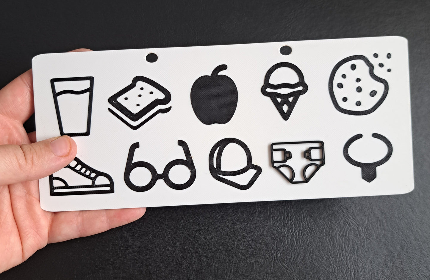 Hand holding a white communication board with black shapes against a black background