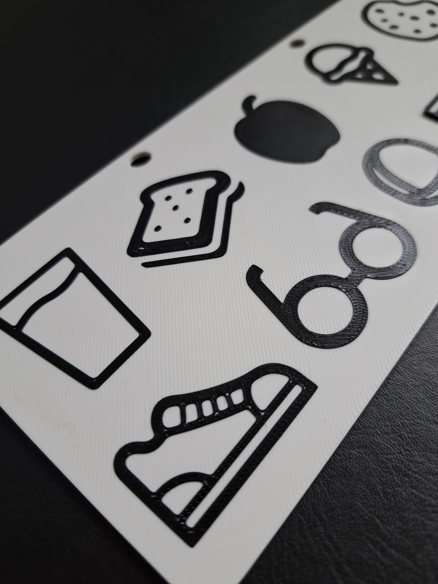 Hand holding a white communication board with black shapes against a black background