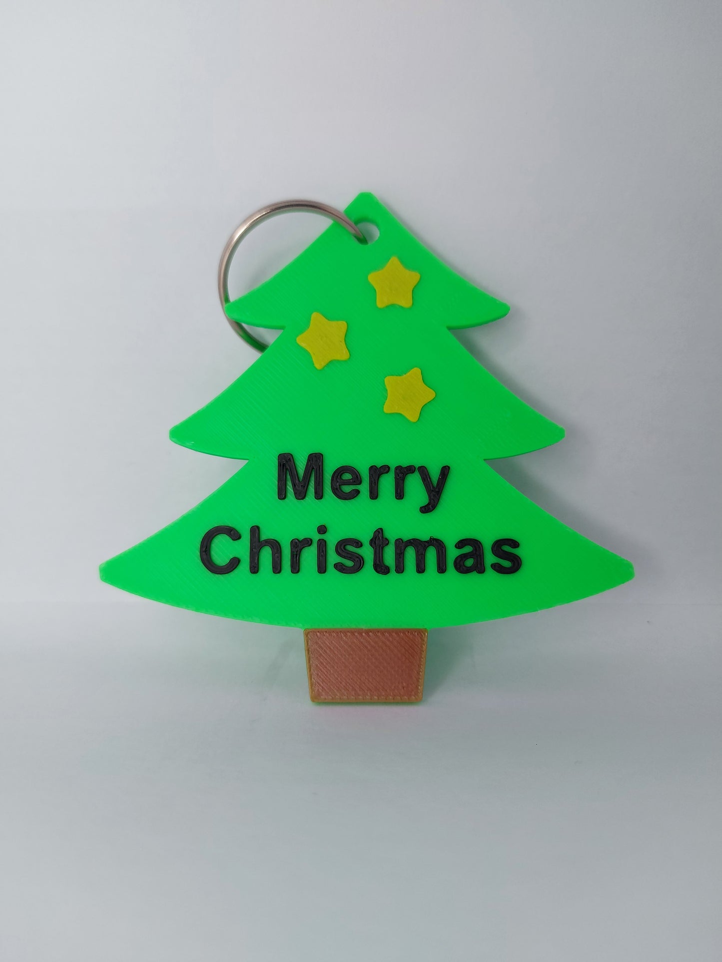Green Christmas tree-shaped keychain with 'Merry Christmas' text and stars on a light gray background