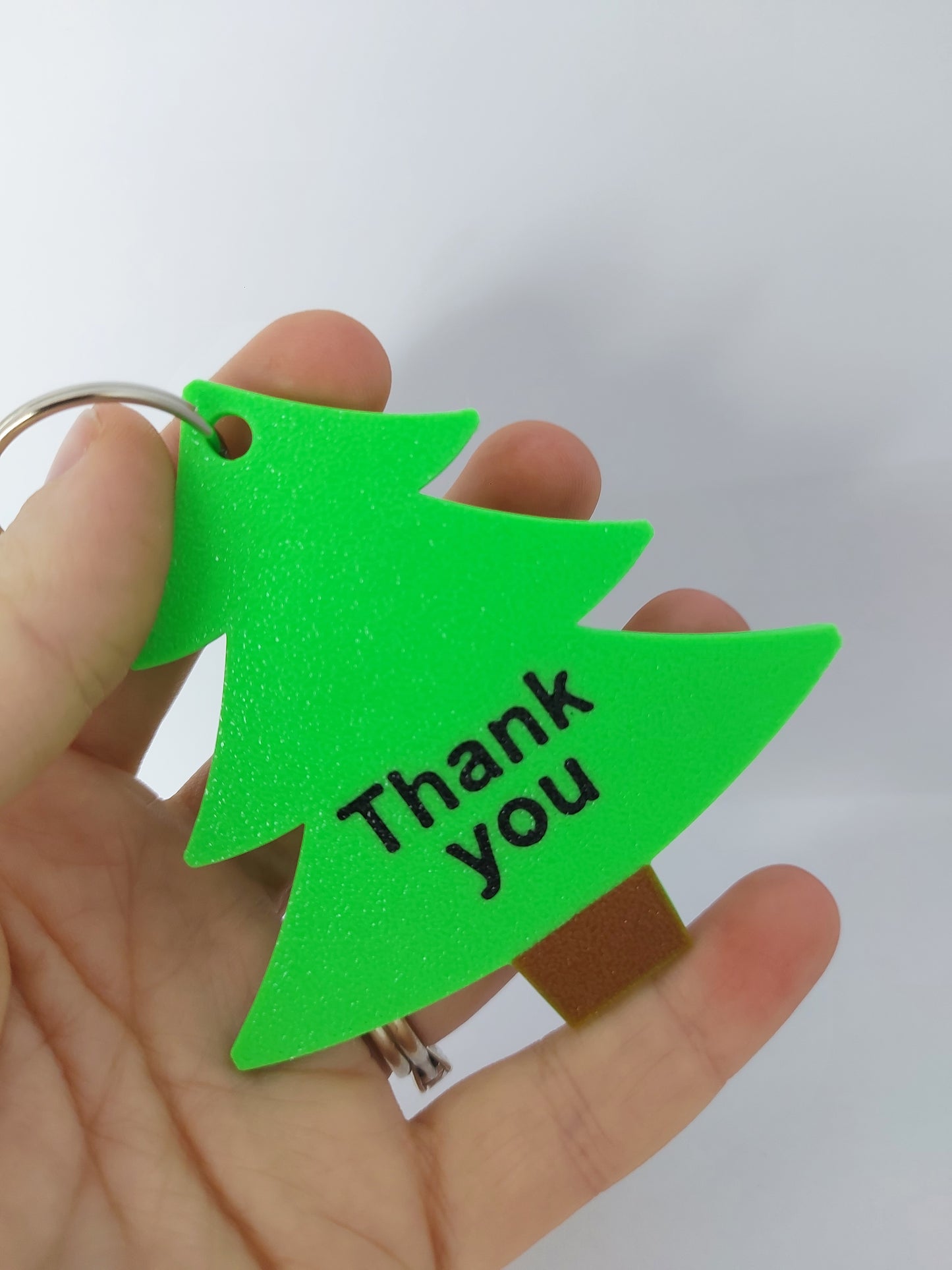 Green triangular keychain with text held in a hand against a white background