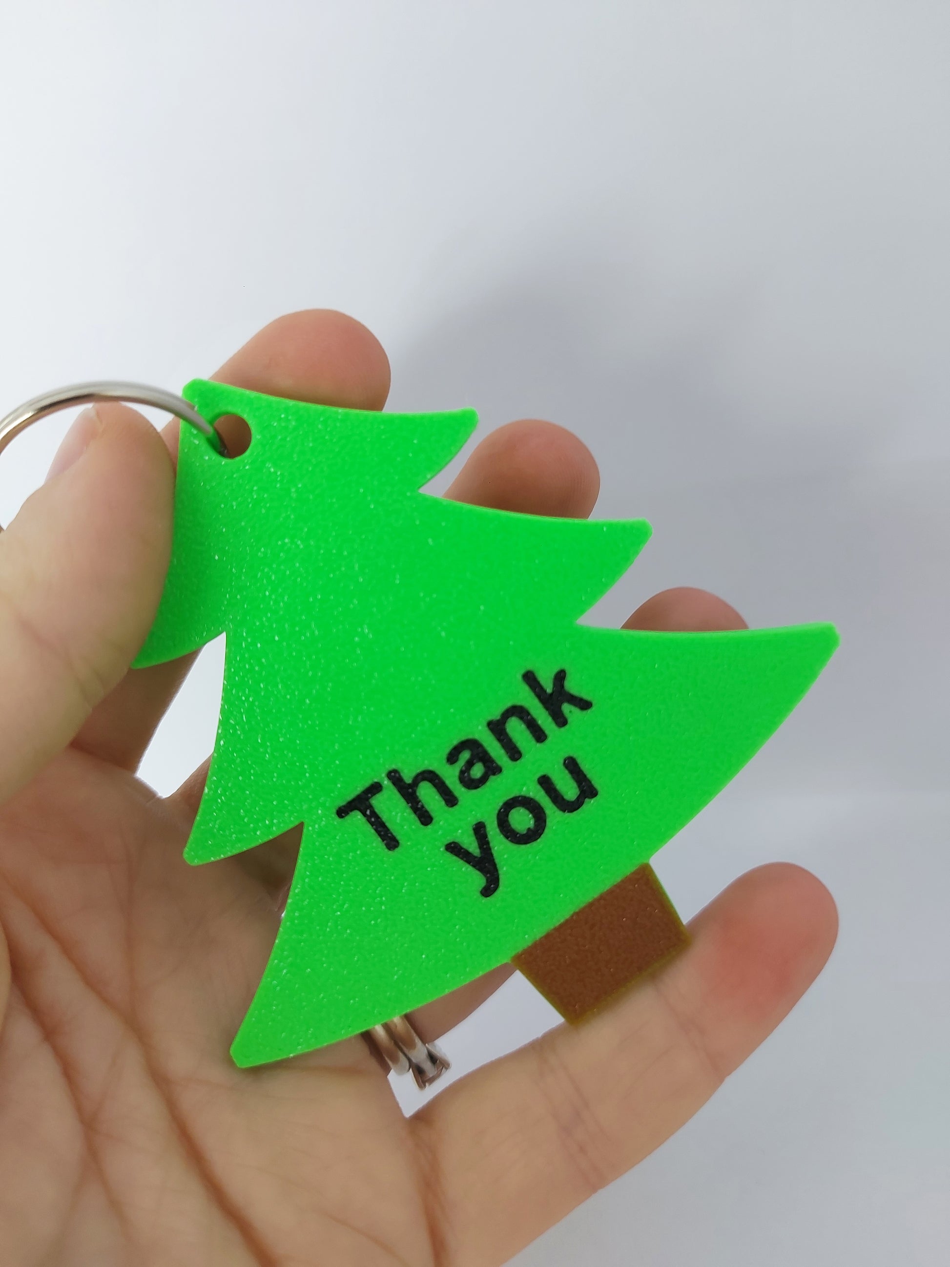 Green triangular keychain with text held in a hand against a white background